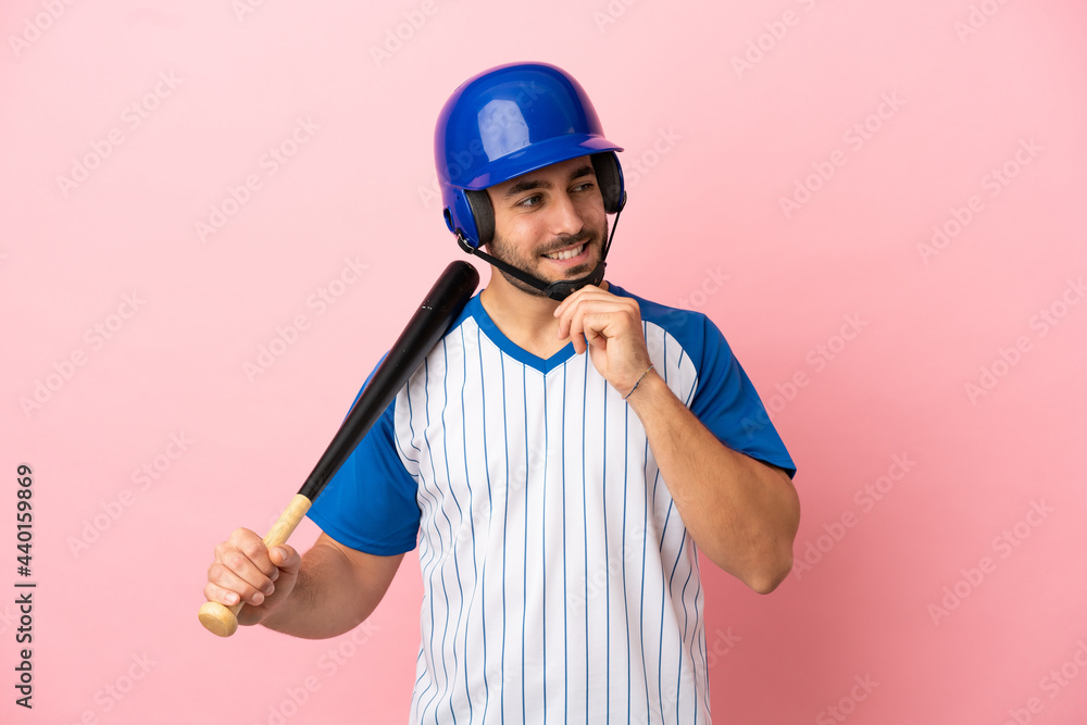 Baseball player with helmet and bat isolated on pink background looking to the side and smiling Baseball player with helmet and bat isolated on pink background looking to the side and smiling