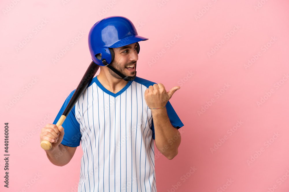 Baseball player with helmet and bat isolated on pink background pointing to the side to present a product Baseball player with helmet and bat isolated on pink background pointing to the side to present a product
