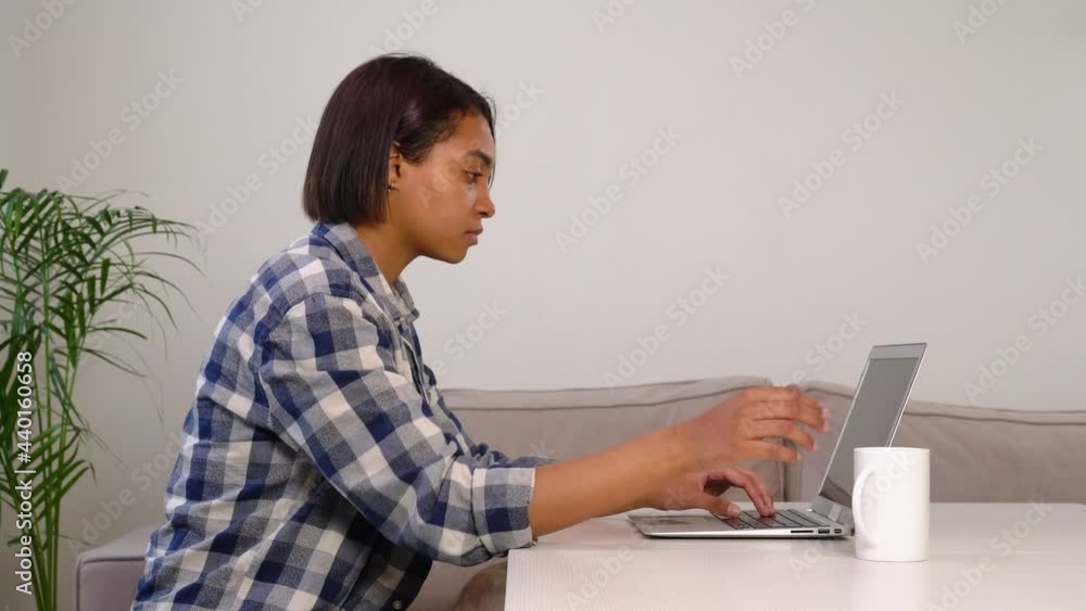 Young beautiful African American woman drinks coffee and works online while sitting at home. The concept of freelancing and working from home. Young beautiful African American woman drinks coffee and works online while sitting at home. The concept of freelancing and working from home.