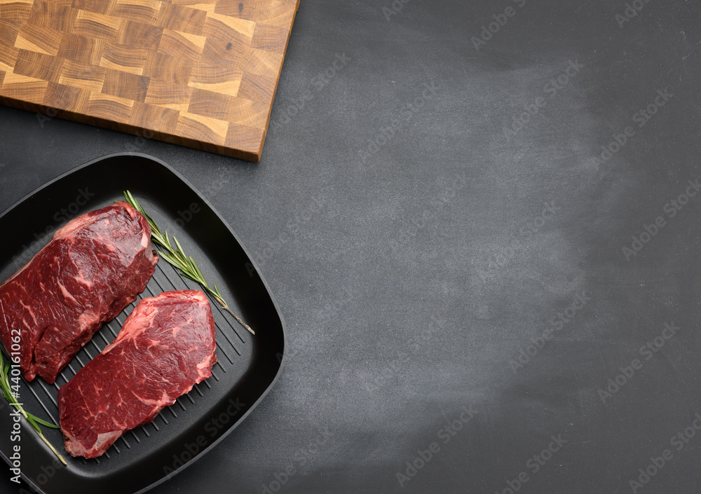 two raw pieces of beef in a black square grill pan, steaks on a black background