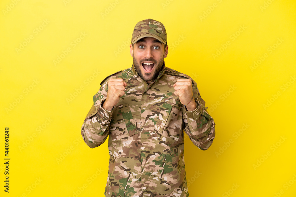Military man isolated on yellow background celebrating a victory in winner position Military man isolated on yellow background celebrating a victory in winner position