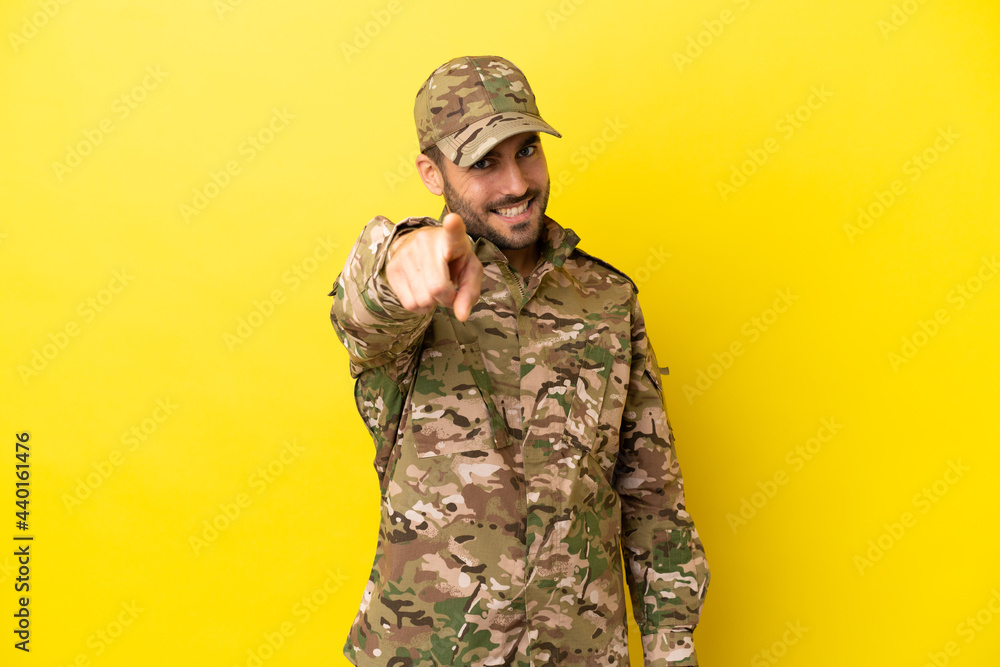 Military man isolated on yellow background points finger at you with a confident expression Military man isolated on yellow background points finger at you with a confident expression