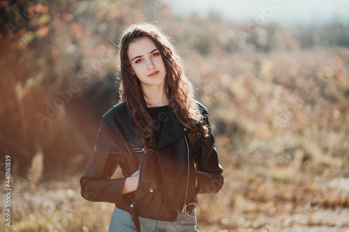 Outdoor portrait of a beautiful teen brunette girl in the black leather jacket