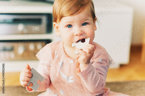 Fotografie Funny toddler 1 year old girl holding puzzle pieces, chewing one part
