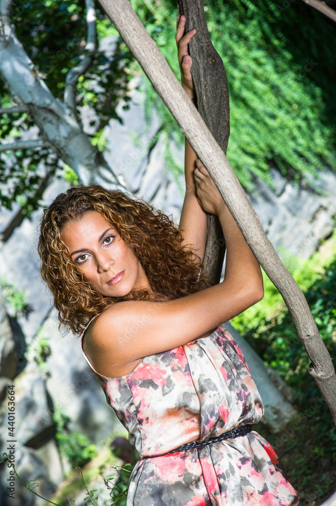 A pretty woman with long brown curly hair is confidently standing in a small woods and looking at you. A pretty woman with long brown curly hair is confidently standing in a small woods and looking at you.