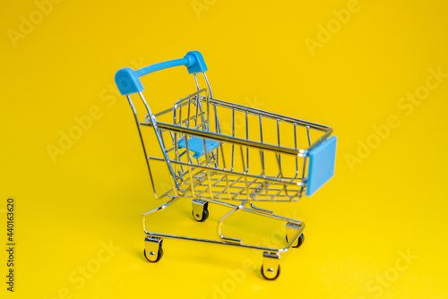 Grocery cart on wheels. Yellow background.