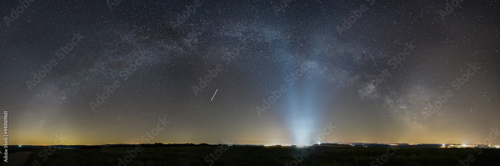 Panorama of Milky Way bow over rural landscape with lights of Spangdahlem Air Base in distance, Germany