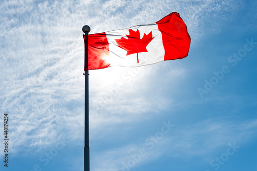canadian flag waving against blue sky and backlit by the sun