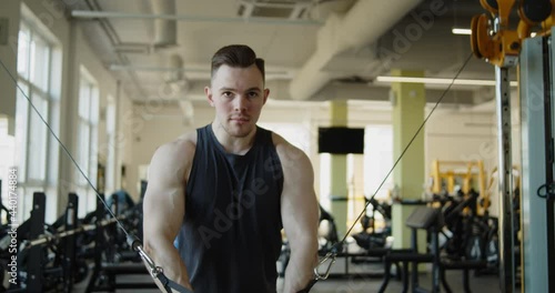 Young attractive muscular athlete works out in a modern gym. Strong fit man doing standing cable crossover exercises during training. Active healthy lifestyle and wellbeing.