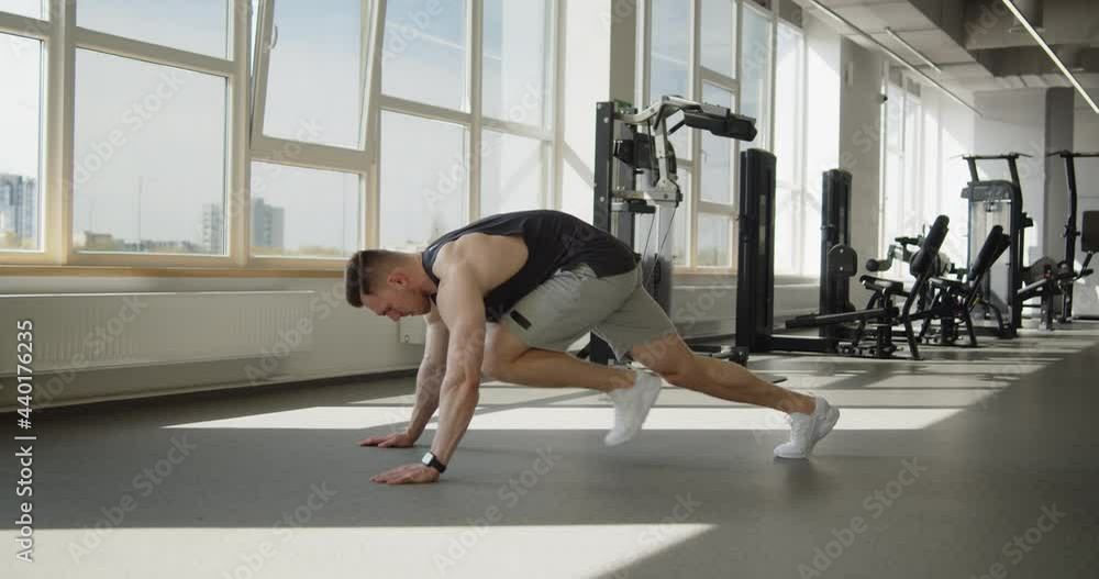 Young attractive muscular athlete works out in a modern gym. Strong fit man doing mountain climbers exercise during training. Active healthy lifestyle and wellbeing. Young attractive muscular athlete works out in a modern gym. Strong fit man doing mountain climbers exercise during training. Active healthy lifestyle and wellbeing.