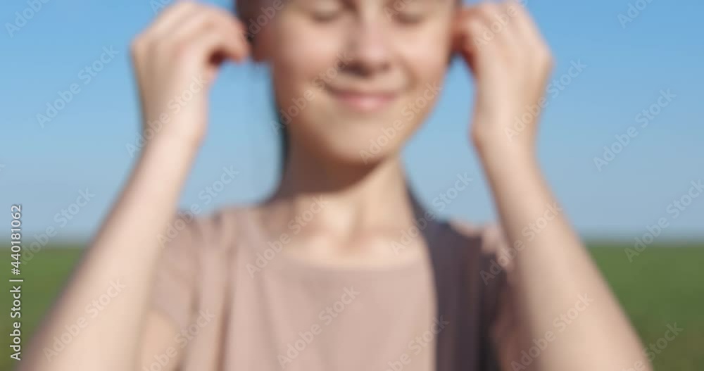 Teen hold a headphones outdoor. A nice teen show her new wireless earbuds and puts in her ears the device. Teen hold a headphones outdoor. A nice teen show her new wireless earbuds and puts in her ears the device.