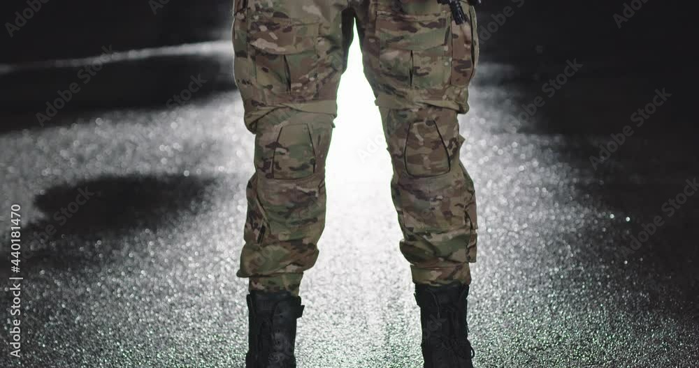 A soldier in a special war uniform, helmet and gloves stands in the dark leaning against a rifle A soldier in a special war uniform, helmet and gloves stands in the dark leaning against a rifle
