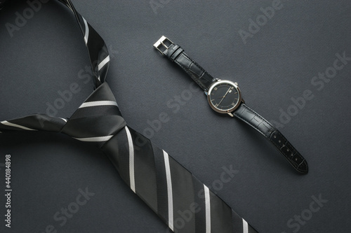 Black and white tie and classic wristwatch on a black background. Flat lay.