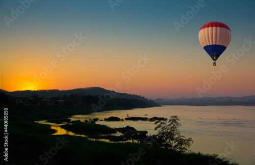Hot air balloon flying over the Mae Kong river with scenic view of sunset in background in Northeast Thailand. © Itsanan