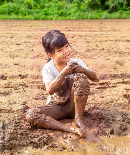 portrait of a little adorable Asian girl sitting smiling and playing in the mud with fun. Family, healthy child, happiness concept