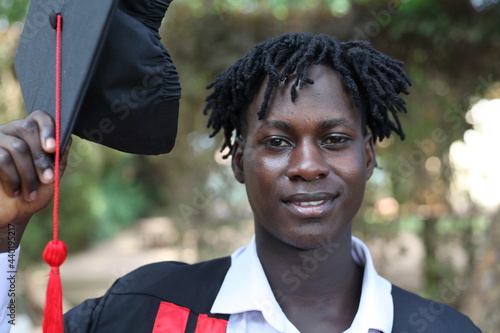 The African American gentle office young business Rasta man graduates and poses for a photo with his graduation cape in his hands and his background is in blur