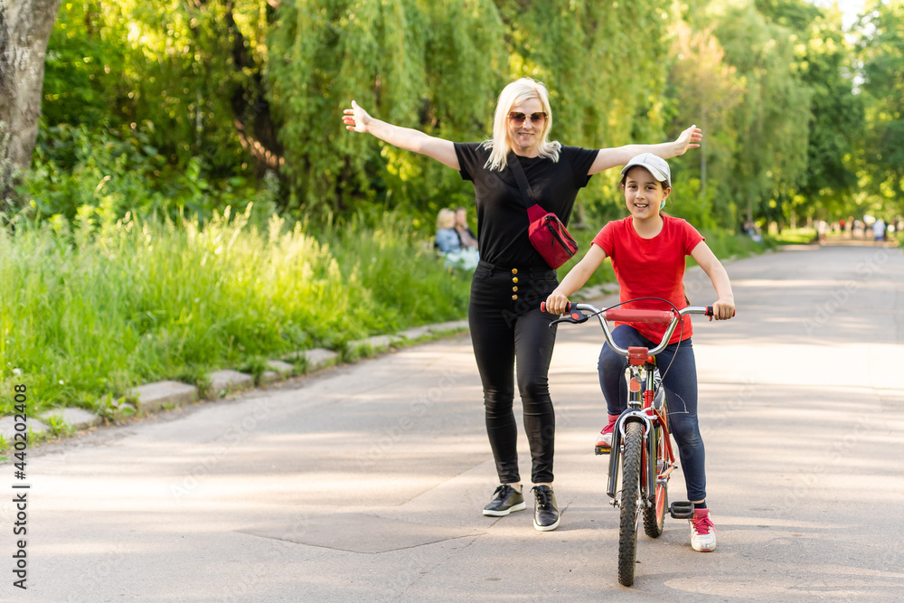 Fototapeta premium Front view portrait of caucasian mother looking through her glasses while helping her daughter to ride the bike
