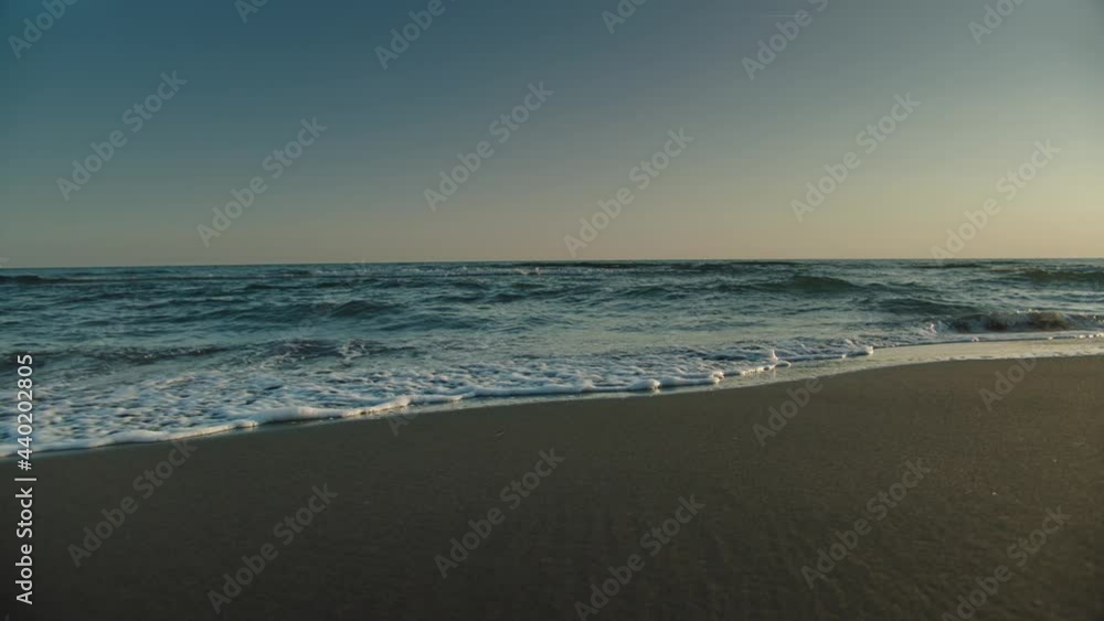 Slide and pan reveal of sea waves washing empty sandy beach in sunset time. Summer evening at seaside. Slide and pan reveal of sea waves washing empty sandy beach in sunset time. Summer evening at seaside.