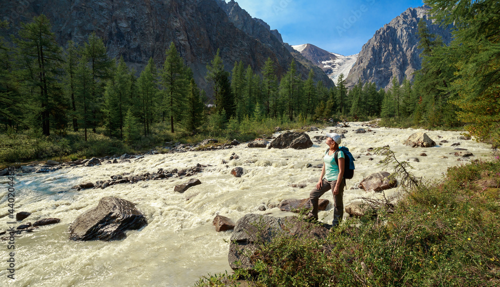 Photo of a tourist girl in the Altai Mountains. In the background is a river flowing from the Bolshoy Aktru glacier, one of the oldest glaciers in the Altai Mountains.