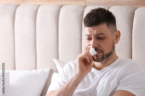 Man suffering from runny nose in bed. Space for text