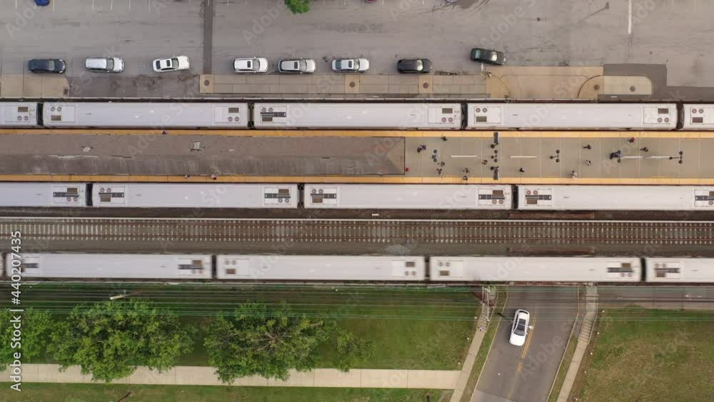A top down shot directly over three trains at a station. One train is pulling out, the others have stopped. Some people are on the platform in the evening. The camera truck right slowly. A top down shot directly over three trains at a station. One train is pulling out, the others have stopped. Some people are on the platform in the evening. The camera truck right slowly.