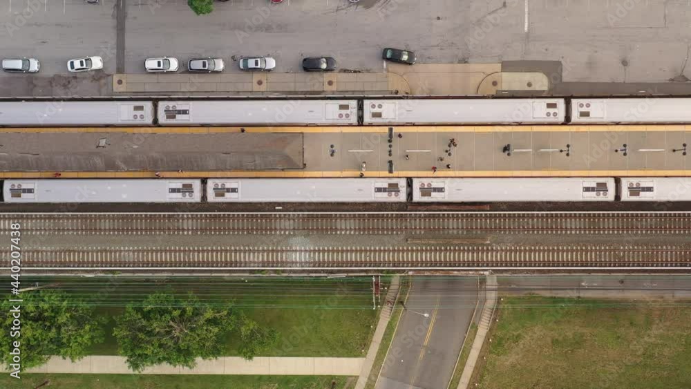 A top down shot directly over two trains parked at a station in the evening. There are people on the platform, with the camera looking straight down, it truck right along the tracks. A top down shot directly over two trains parked at a station in the evening. There are people on the platform, with the camera looking straight down, it truck right along the tracks.