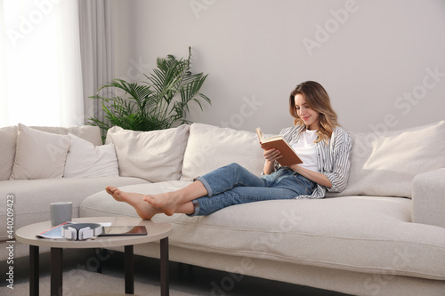 Young woman reading book on sofa at home photo