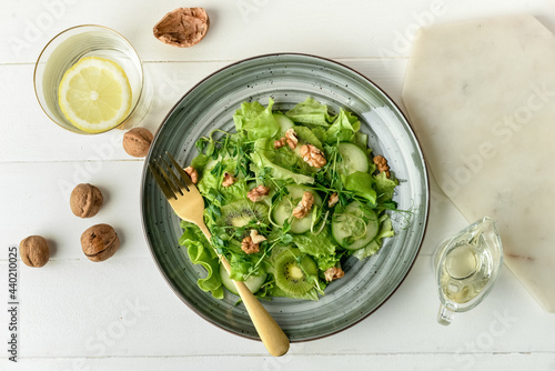 Plate with fresh salad and walnuts on light wooden background