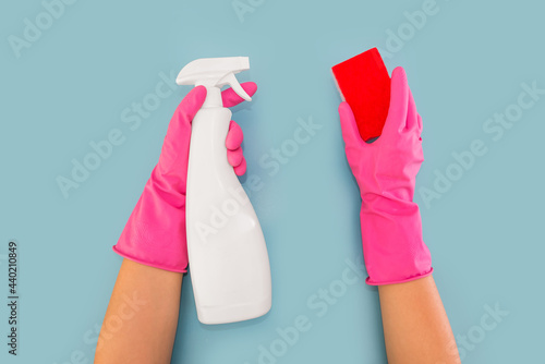 hands in pink gloves hold a detergent dispenser and a washcloth. Blue background.