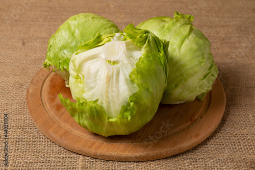 three heads of iceberg lettuce lies on a round wooden board, against a background of linen cloth, close-up