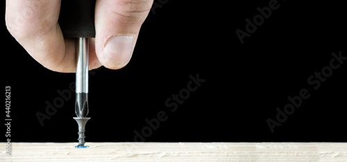 Banner with screwdriver twists the self-cut into wooden boards close up isolated on black background with space for text.