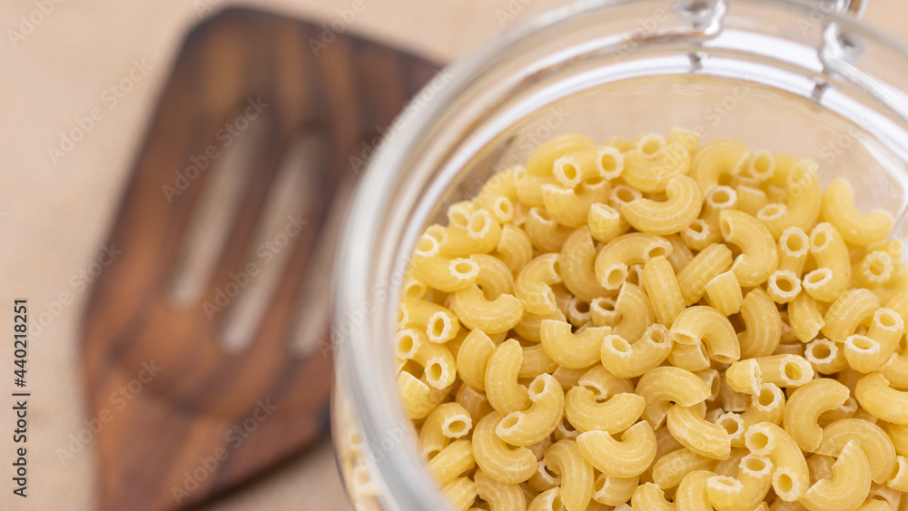 The uncooked macaroni in the opened bottle with the blurred wooden turner in the background The uncooked macaroni in the opened bottle with the blurred wooden turner in the background