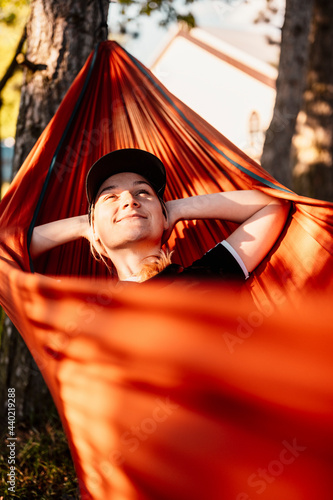 Woman with cap resting in comfortable hammock during sunset. Relaxing on orange hammock between two trees pine enjoying the view photo