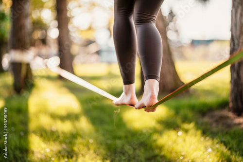 Slacklining is a practice in balance that typically uses nylon or polyester webbing. Girl walking on a slackline in a park during a sunset. Slack line photo