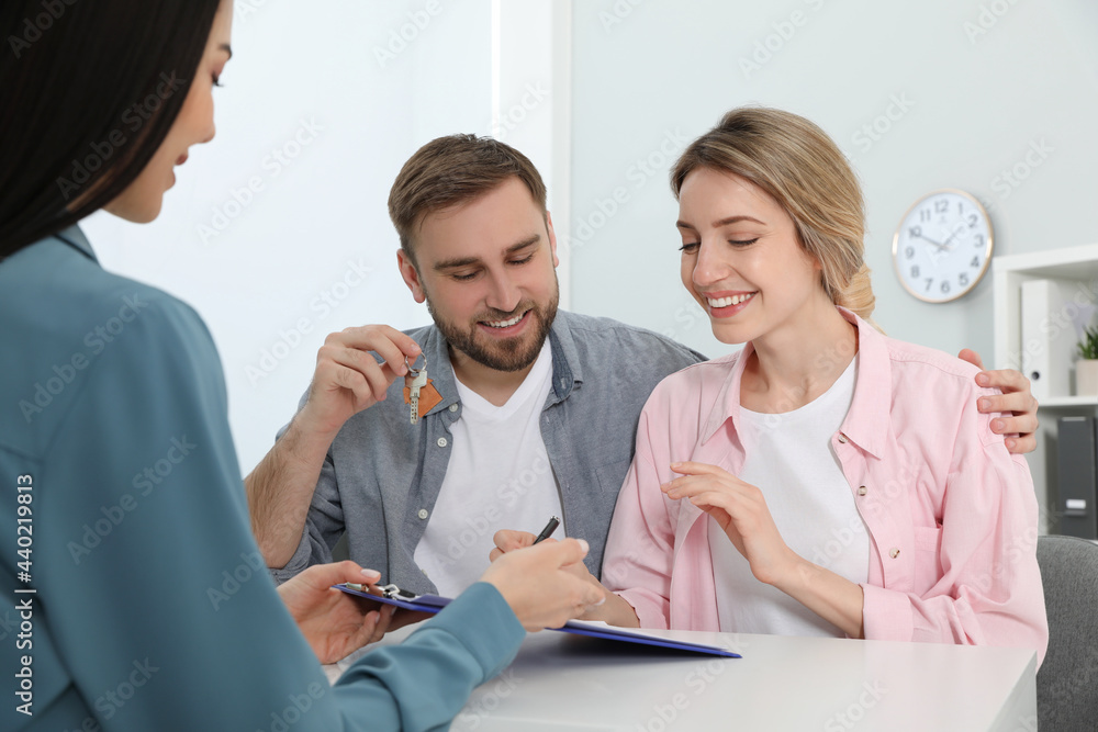 Happy young couple signing purchase contract in real estate agent's office. Man with new house key Happy young couple signing purchase contract in real estate agent's office. Man with new house key
