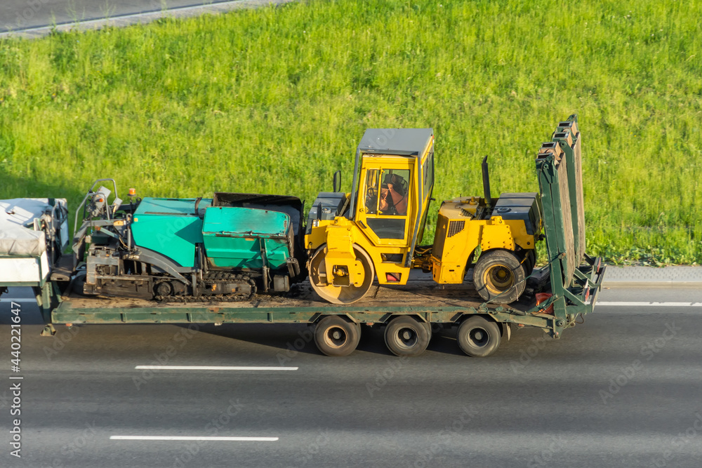 Transporting the road roller and asphalt paver on the cargo platform by the truck trailer. Transporting the road roller and asphalt paver on the cargo platform by the truck trailer.