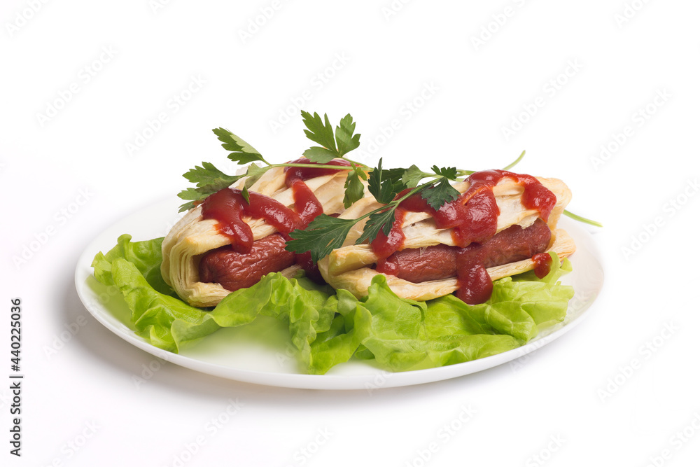 two appetizing sausages in a dough on a white plate with fresh lettuce leaves, parsley and ketchup