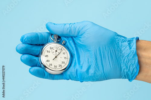 Stopwatch in the hand of a doctor in a glove on a blue background. Fast medical aid concept