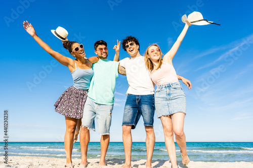 Group of multiracial young tourists posing for portrait photography in summer at tropical sea ocean resort with blue sky and crystal clear water. Happy millennial people on summer beach vacation