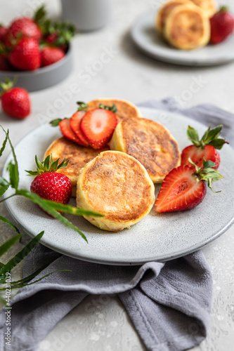 Cottage cheese pancakes or fritters with strawberry and natural yogurt on light grey stone background. Healthy breakfast or lunch. Syrniki.
