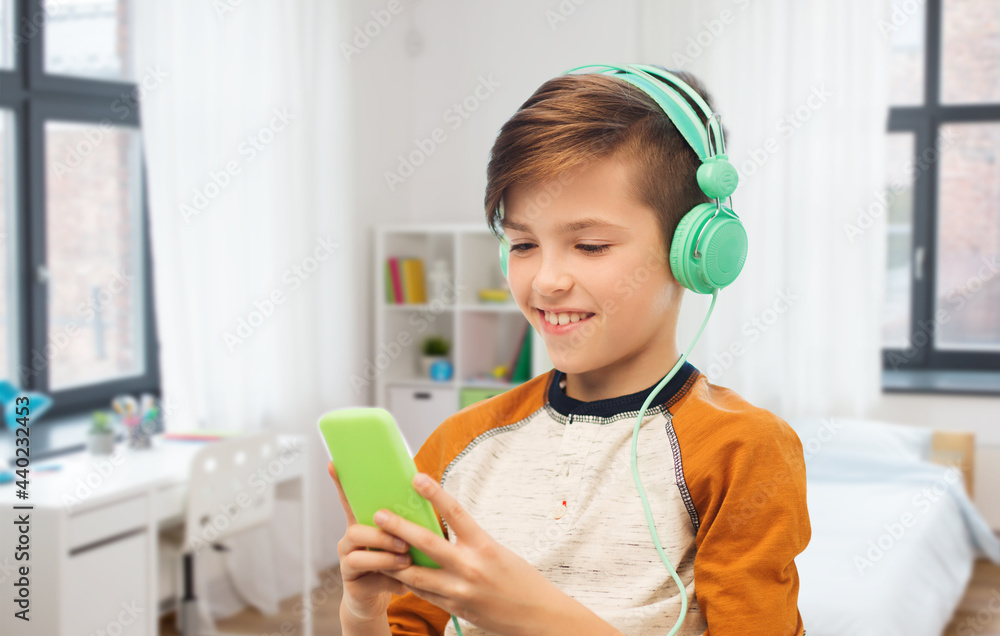 leisure, technology and people concept - happy smiling boy with smartphone and headphones listening to music at home over children's room background leisure, technology and people concept - happy smiling boy with smartphone and headphones listening to music at home over children's room background