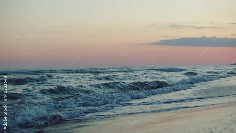 Low angle view of rolling and splashing waves washing beach after sunset. Pink twilight sky. Summer evening at seaside. Low angle view of rolling and splashing waves washing beach after sunset. Pink twilight sky. Summer evening at seaside.