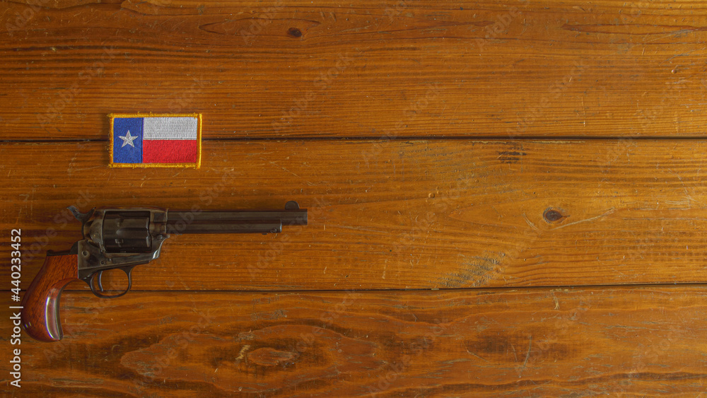 Single action revolver below a Texas state flag patch on a textured wooden plank background
