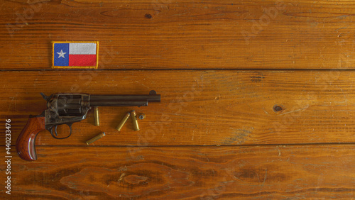 Single action revolver, with ammunition, below a Texas state flag patch, on a textured wooden plank background