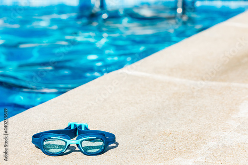 Blue swimming goggles on the curb of the pool, in the lower left corner, with the blue water in the background