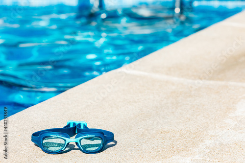 Billede på lærred Blue swimming goggles on the curb of the pool, in the lower left corner, with th