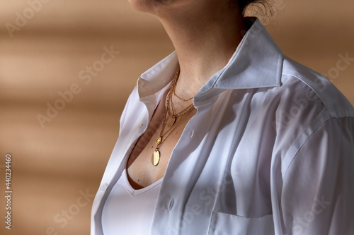 beauty, fashion and jewelry trends concept - close up of woman in white shirt wearing golden multi layer necklace with coin medallions photo