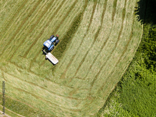 drone shot of blue tractor with mower cutting fresh green meadow somewhere in austria
