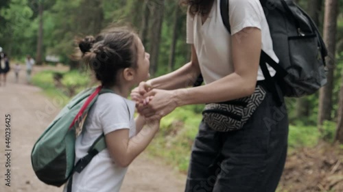 Happy smiling cute daughter jumping around her young mother in the forest park holding hands together. Happiness being together, kid dream, freedom or family vacation together concept. Slow motion