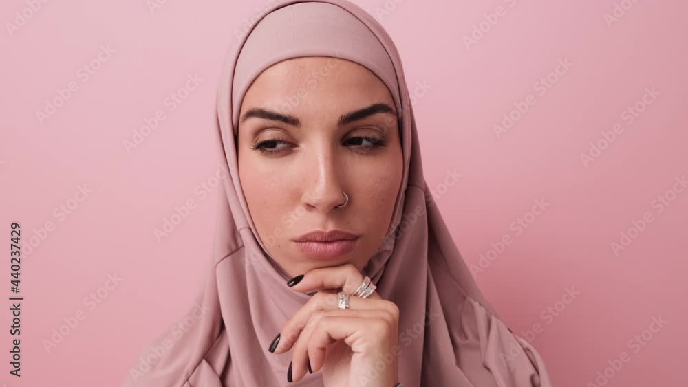 A close-up view of a beautiful arabian woman is thinking about something standing isolated over a pink wall in the studio A close-up view of a beautiful arabian woman is thinking about something standing isolated over a pink wall in the studio